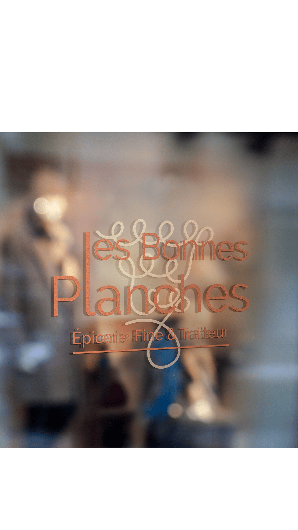 Logo Les Bonnes Planches appliqué en lettrage sur la vitrine d'une épicerie fine.