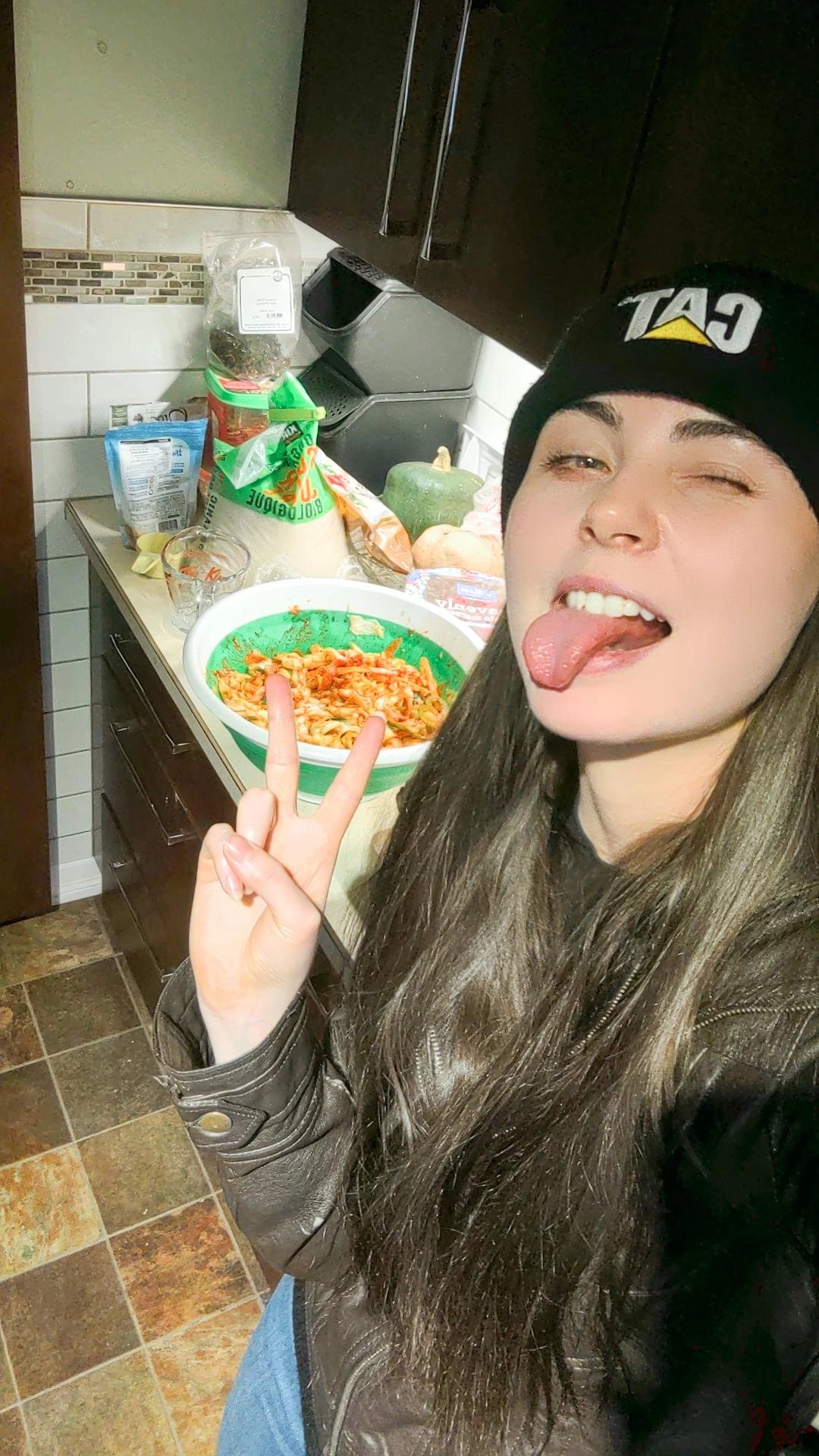 a woman with long hair and a hat on with her tongue stuck out in front of kimchi