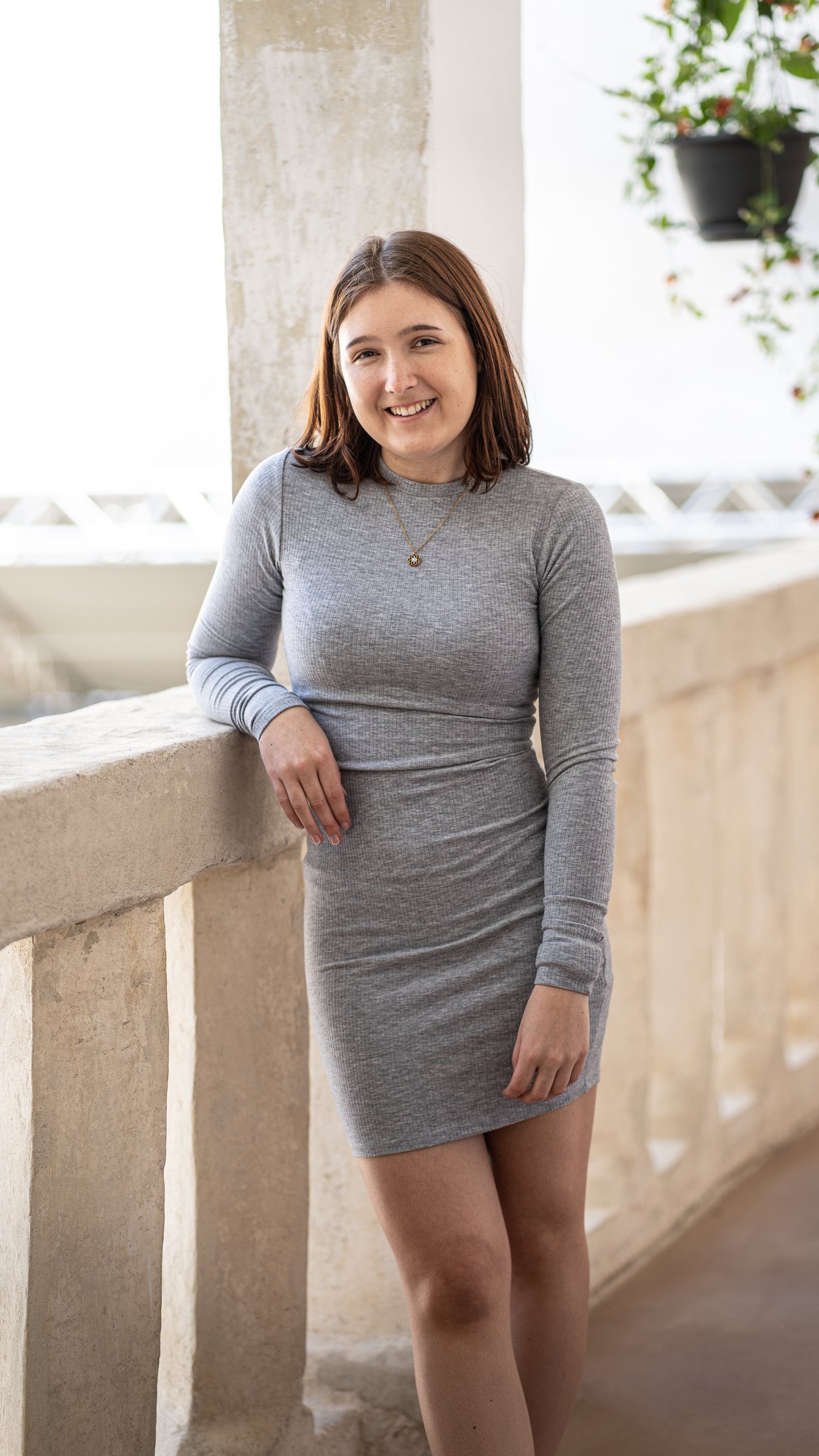 eine Frau in einem grauen Kleid, dass sich locker anlehnt und in die Kamera schaut