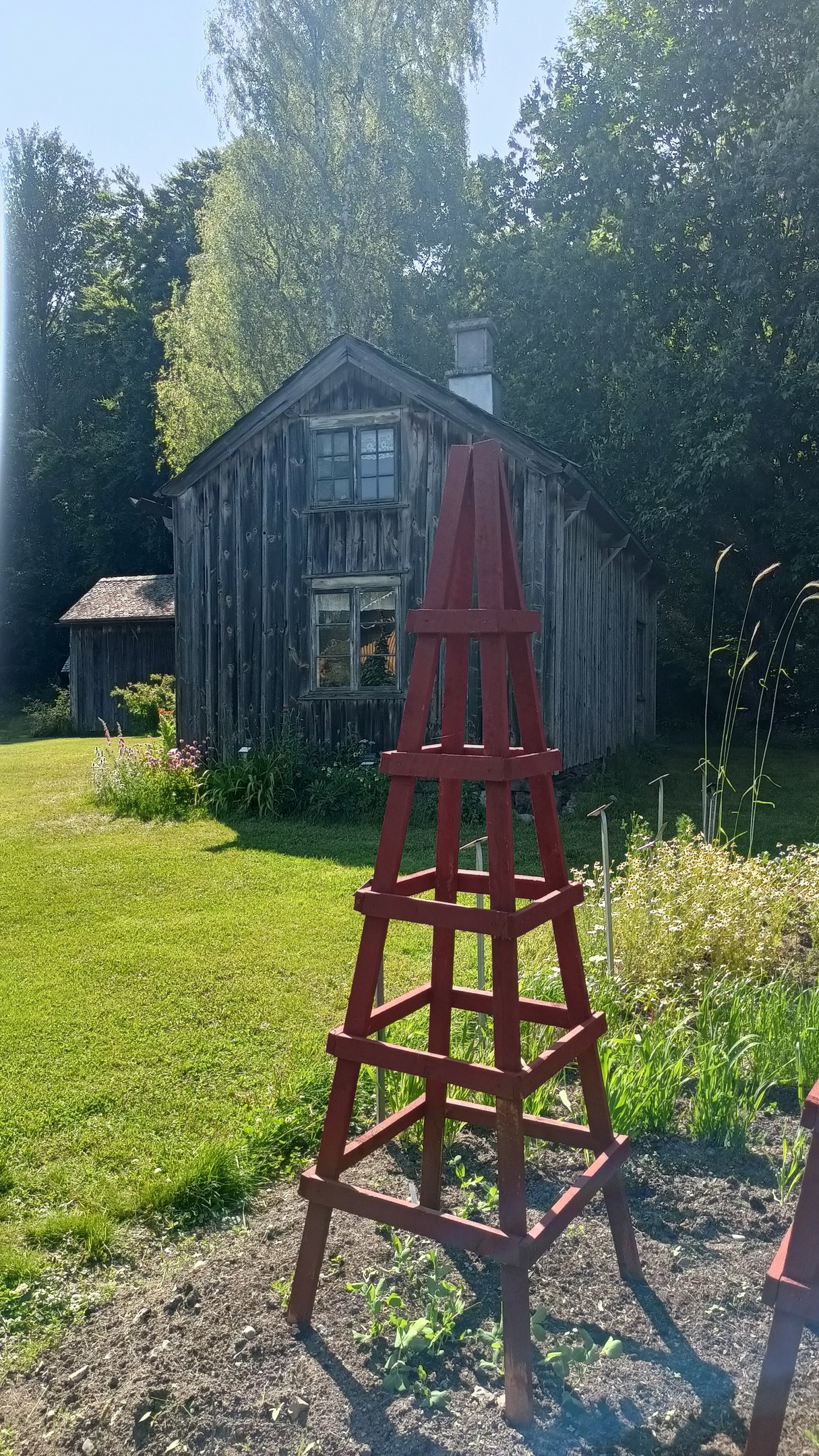 un tuteur de jardin peint en peinture naturelle suédoise en forme pointue devant une vieille maison en bois