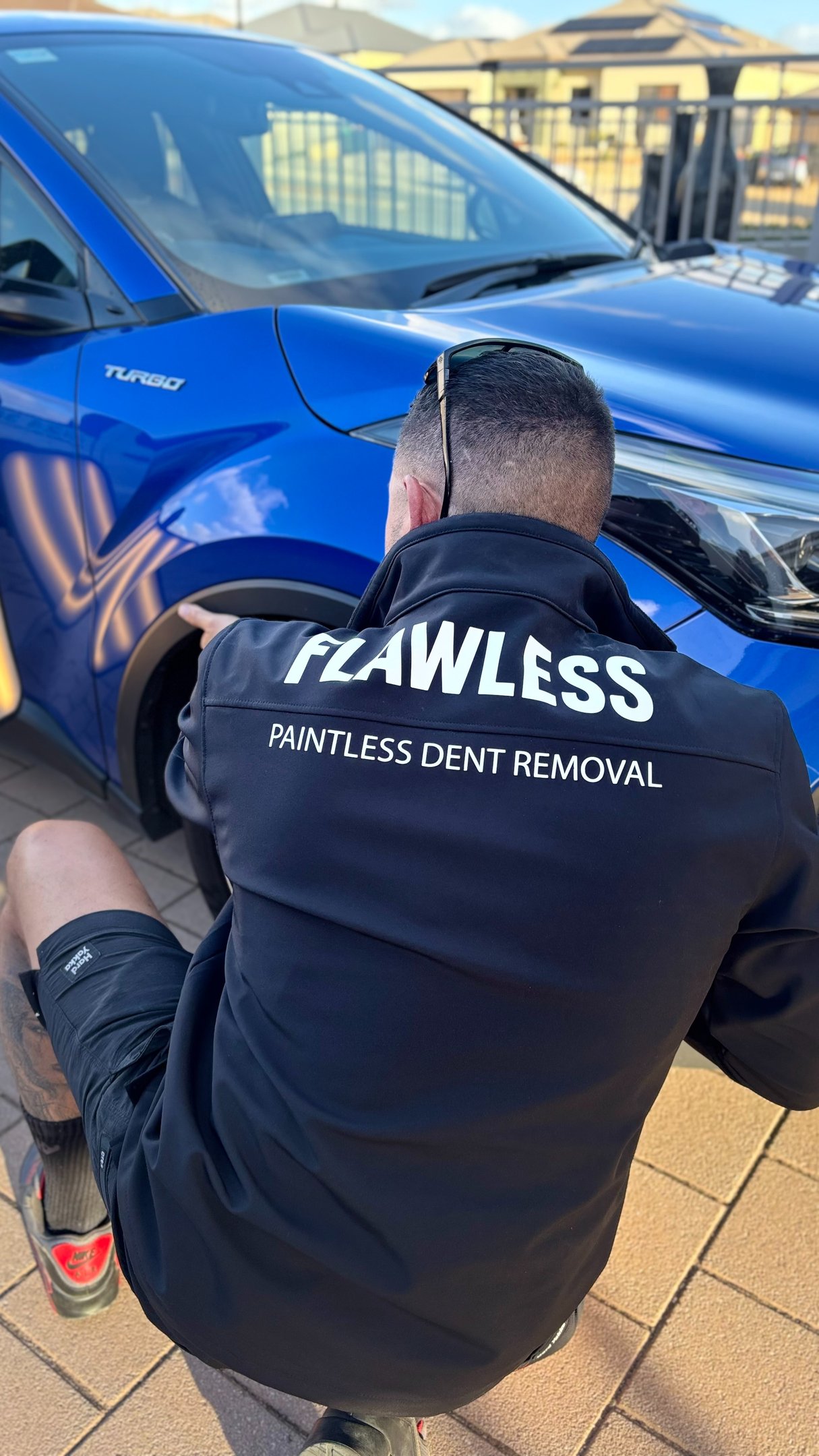 Professional technician performing paintless dent removal on a blue car fender.