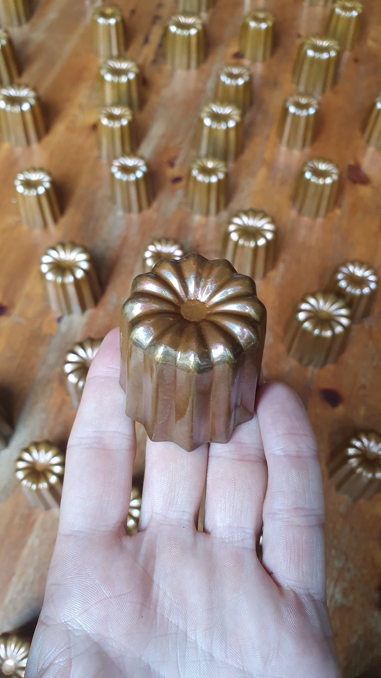 Un moule à cannelé en cuivre tenu dans une main