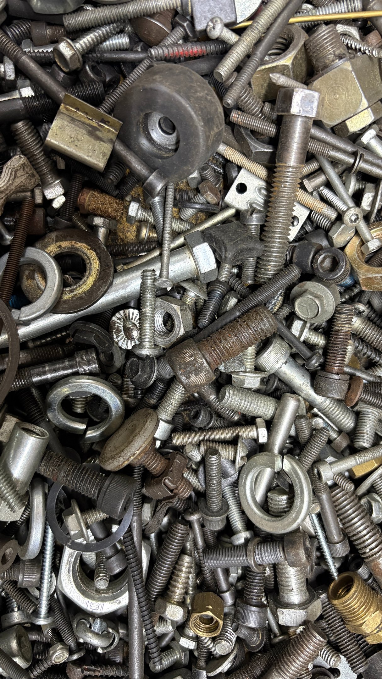 Top view of a disorganized pile of various metal fasteners, including steel bolts, nuts, screws, and washers.