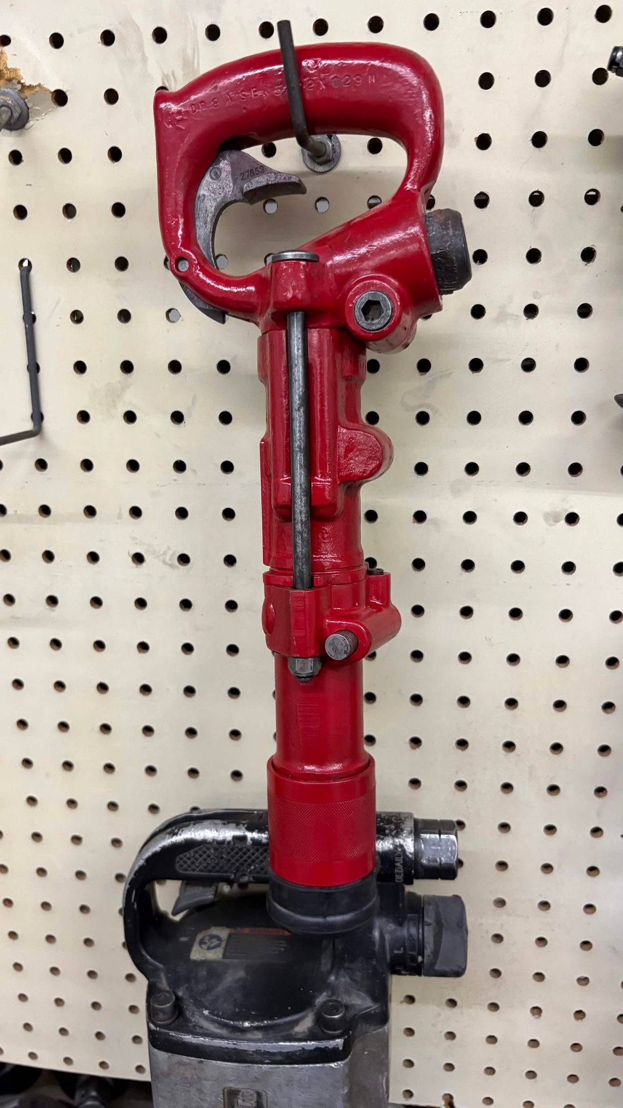 Red industrial pneumatic rivet buster tool hanging on a pegboard in a workshop.