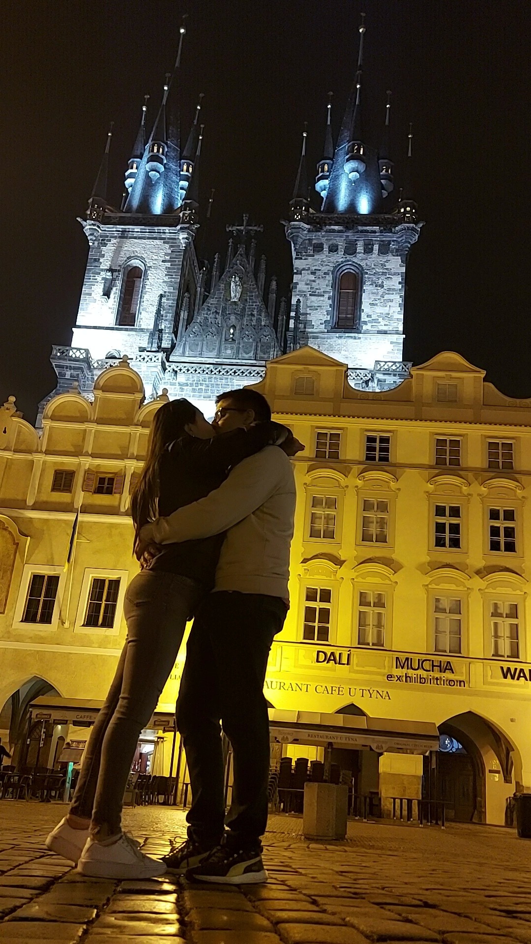 Pareja abrazándose frente a la Iglesia de Týn iluminada por la noche en Praga.