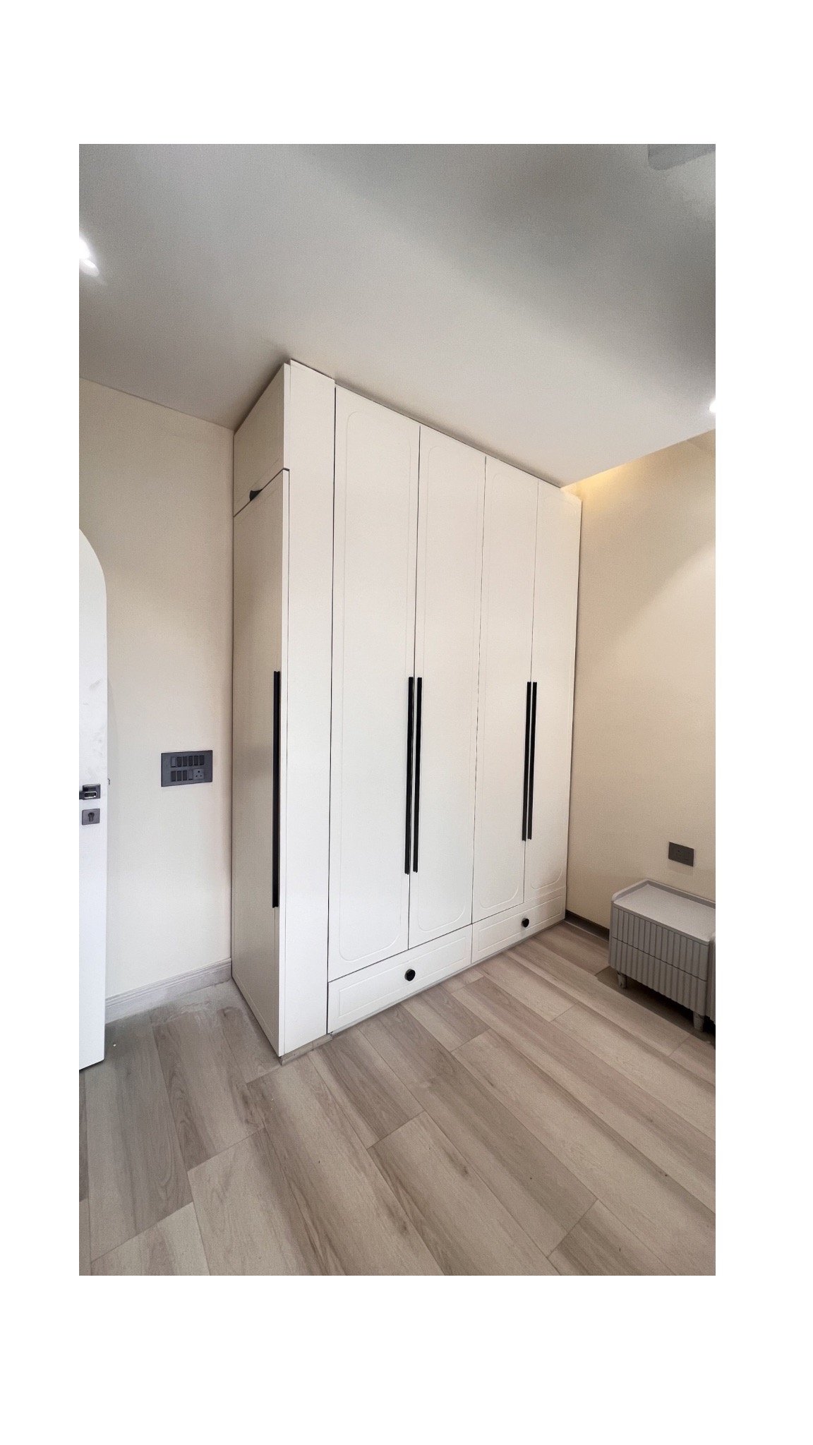 Modern white floor-to-ceiling built-in wardrobe with long black handles in a minimalist bedroom.