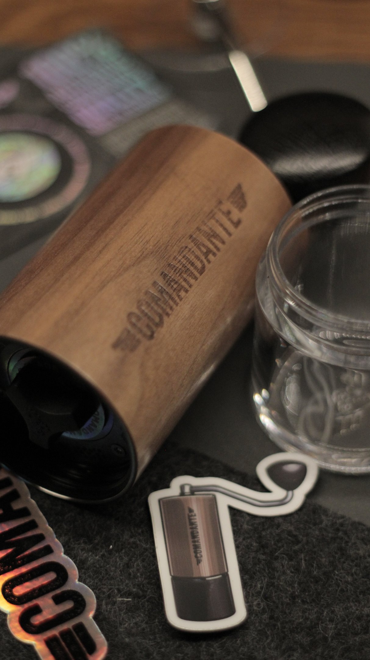Comandante wood manual coffee grinder next to a glass jar and stickers for specialty coffee brewing.