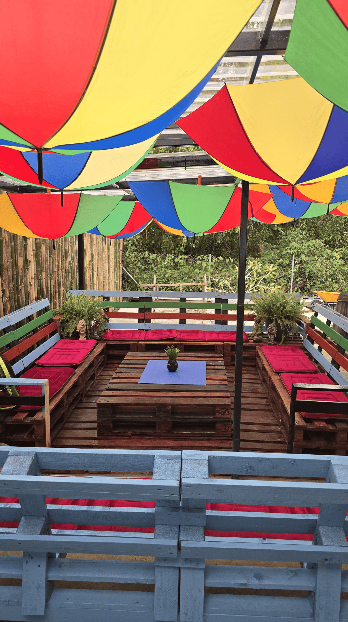 Outdoor patio lounge with colorful umbrella ceiling and DIY pallet furniture seating area.