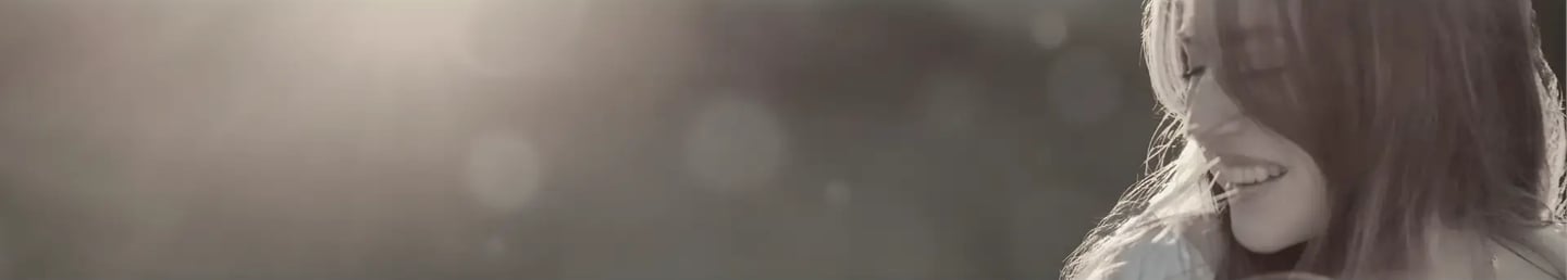 A smiling young woman enjoying sunlight in a soft-focus, dreamy outdoor setting.