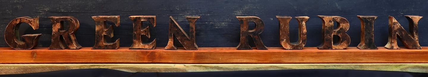 Kunstvoller Schriftzug der Marke Green Rubin in dunkel bemalten Lettern auf einem Holzbalken