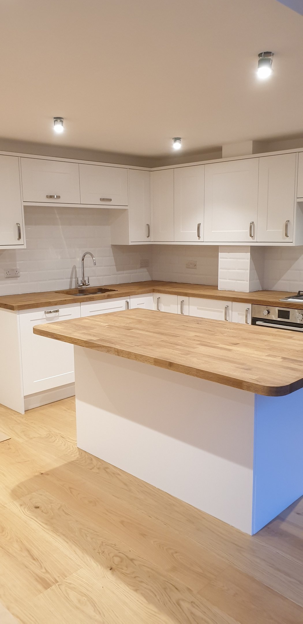 Modern white kitchen featuring a solid oak wood island countertop and matching hardwood flooring.