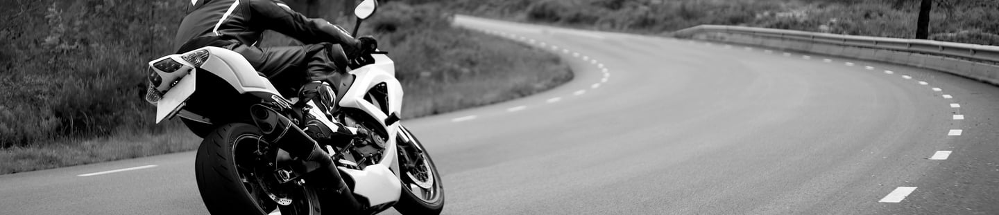 Rear right view of a motorcycle as it take a left hand bend with a road position that gives the view