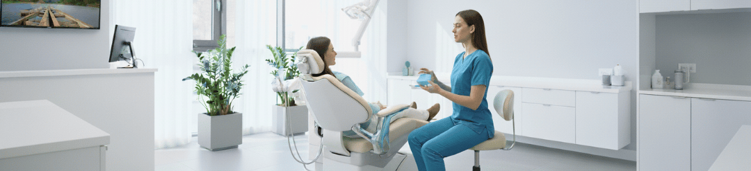 Una dentista con alineadores transparentes explicando el tratamiento a una paciente en el sillón