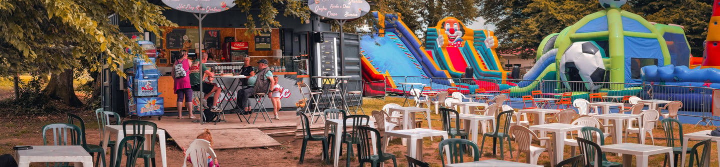 An outdoor food stand with a patio, located next to colorful inflatable slides and bouncy castles.