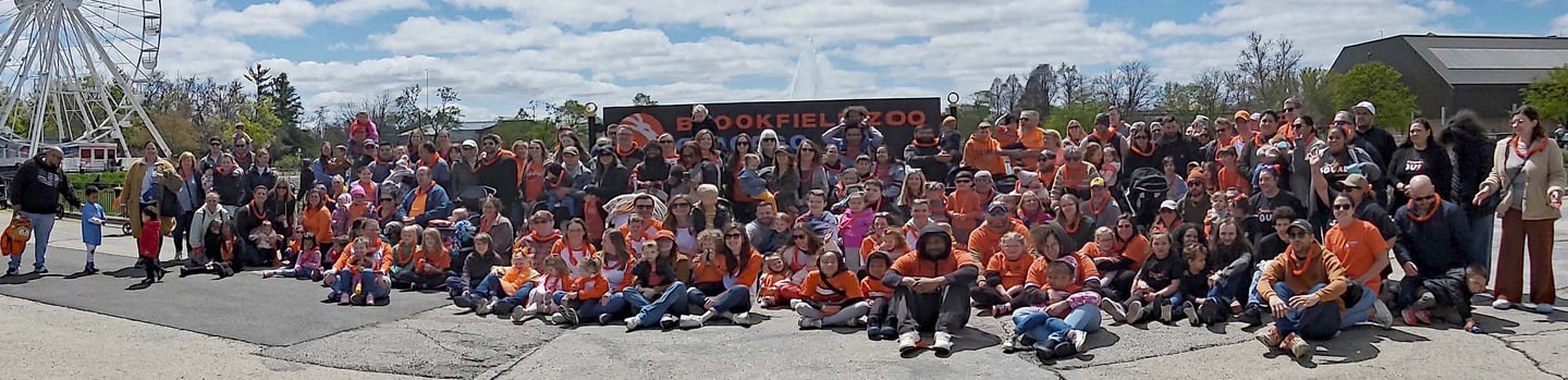 Group of people in orange and mixed color shirts of all ages sizes and colors in front of brookfield zoo sign