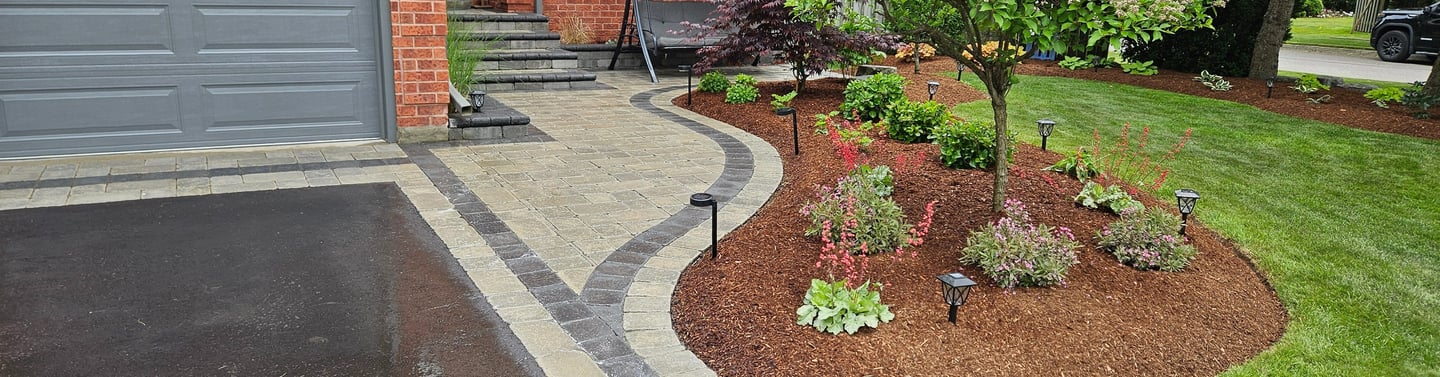 A professionally landscaped front yard featuring a curved interlocking stone walkway and mulch garden beds with ornamental