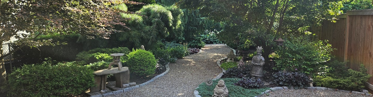 Zen garden backyard with gravel path, Japanese maple trees, and decorative Buddha statues.