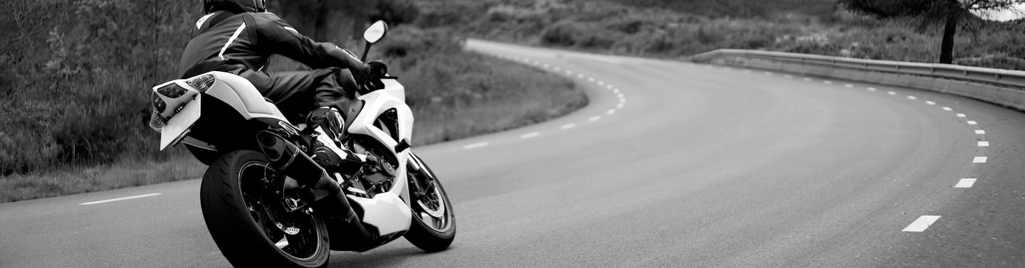 Rear right view of a motorcycle as it take a left hand bend with a road position that gives the view