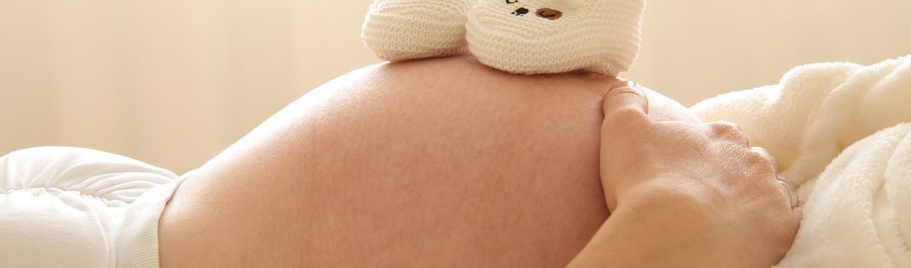 Une femme enceinte tient son ventre et les chaussons de son bébé