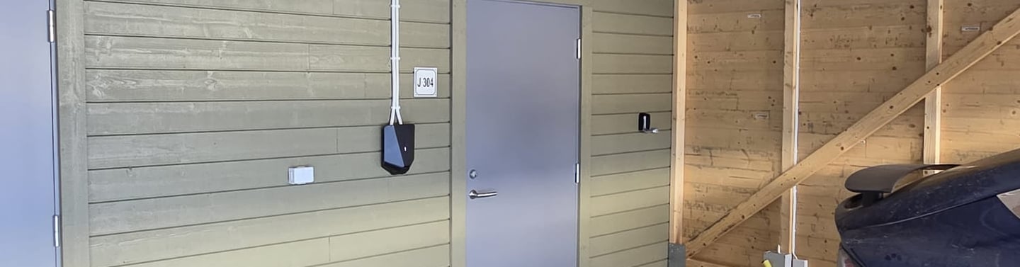 Interior of a modern timber frame carport with a black electric vehicle charging station installed on a wooden wall.