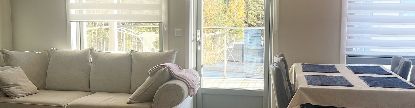 Modern open plan living room featuring a grey sofa, dining table, and zebra blinds on large windows.