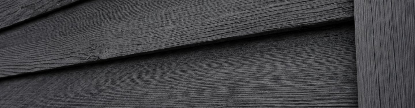 Black wood siding on a traditional barn showing matte, breathable exterior paint aging naturally in shaded conditions