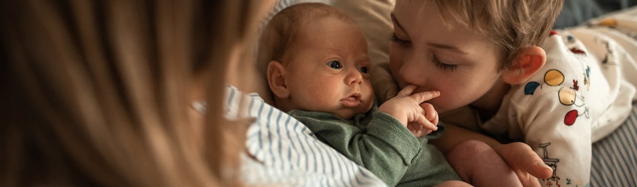a young boy is holding a baby and kissing her hand, best gifts for second-time moms