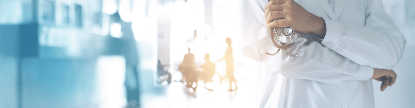 A doctor in a white lab coat holds a stethoscope in a busy hospital hallway.