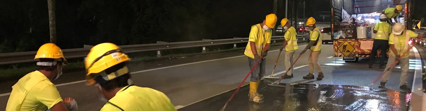 Construction workers in high-visibility vests paving a road with asphalt at night.