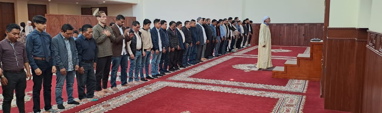 a group of men standing in line performing salat at Imam Malik Mosque