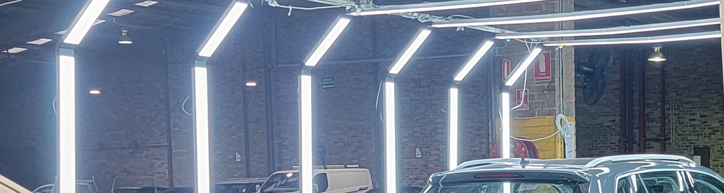 Modern LED arch lighting system illuminating cars in a professional automotive detailing and inspection garage.