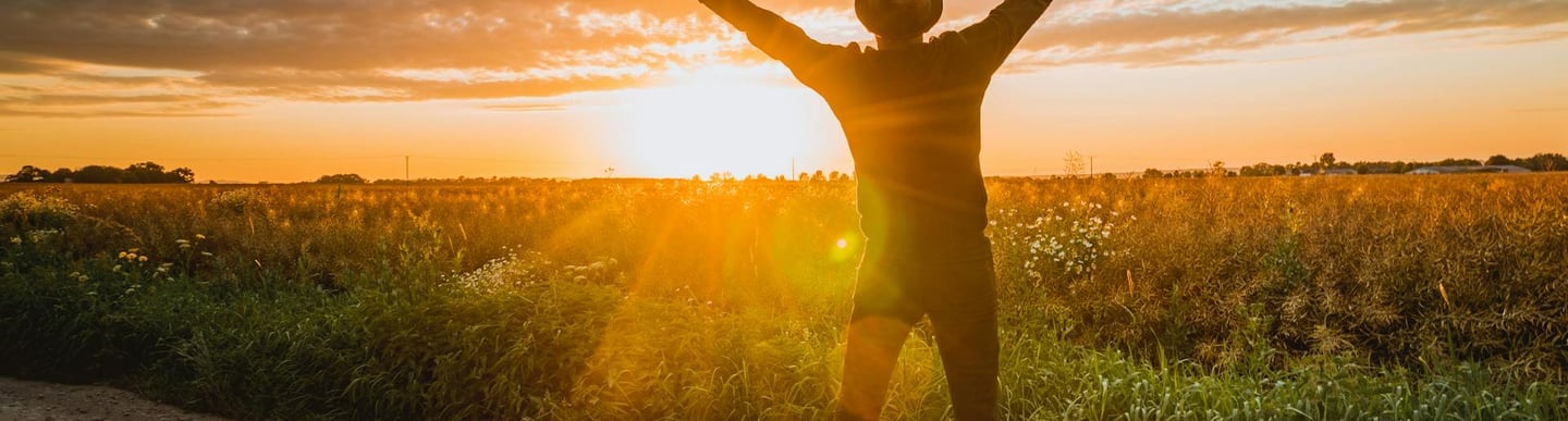 man with uplifted arms looking at sunrise