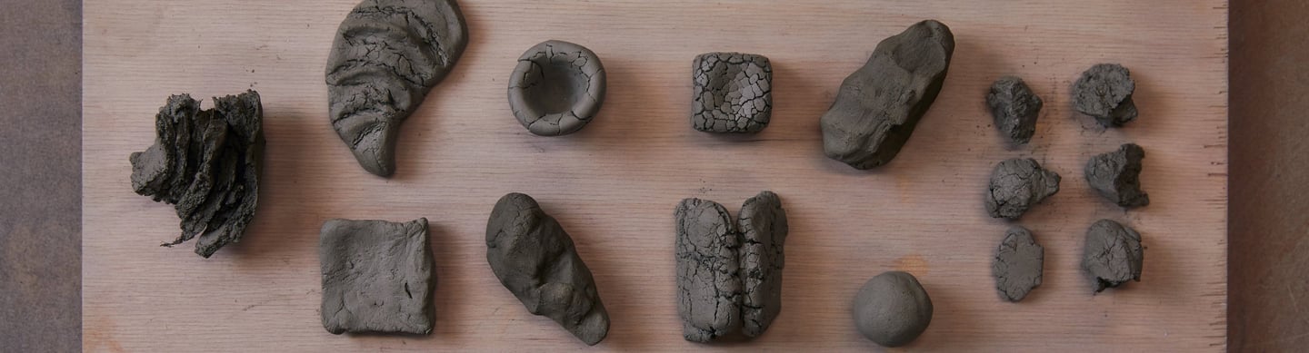 Various sculpted gray clay shapes on a wooden board. The clay was foraged from Devon, UK