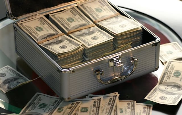 An open silver briefcase filled with stacks of hundred-dollar bills representing wealth and cash flow.
