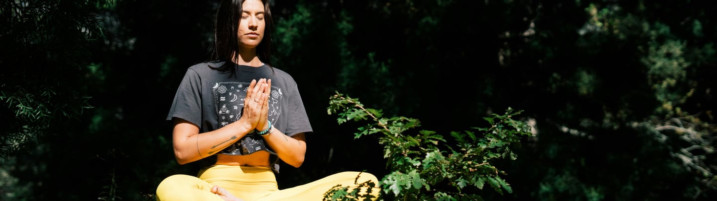 a woman sitting on a rock with her hands clasped in a yoga pose