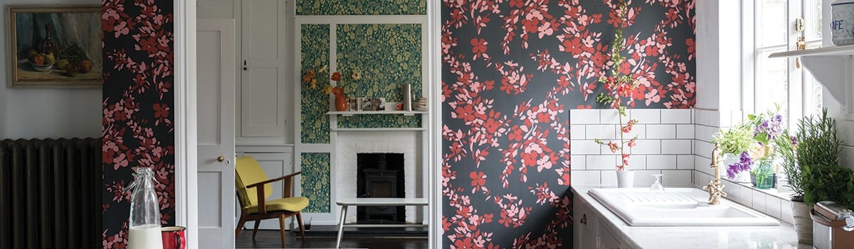 Modern kitchen with red floral wallpaper, marble countertops, and a view into a cozy living room.