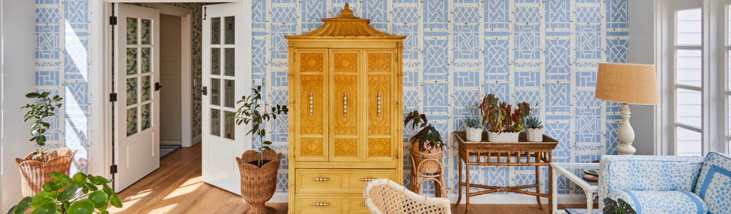 Elegant sunroom featuring blue geometric lattice wallpaper, an ornate yellow Chinoiserie armoire, and lush indoor plants.