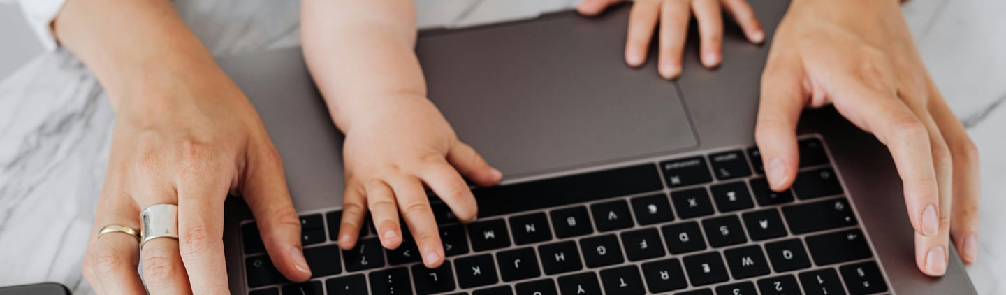a mother typing on a laptop with a baby's hands also on the keyboard