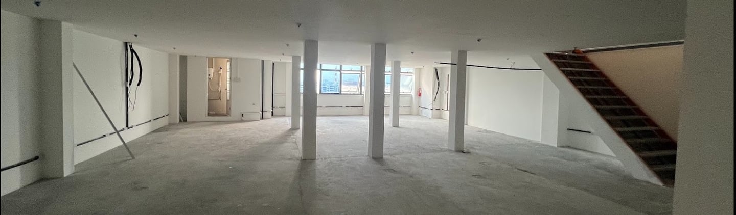 Empty commercial office space with white walls, concrete floors, support pillars, and a staircase.