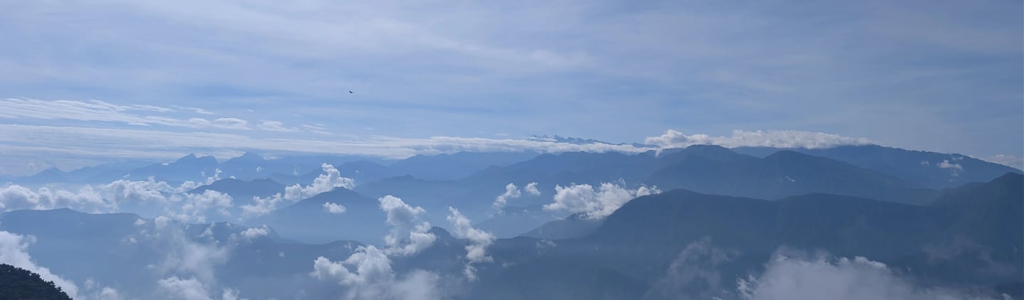 Panoramic mountain range view with blue misty peaks and white fluffy clouds under a bright sky. 