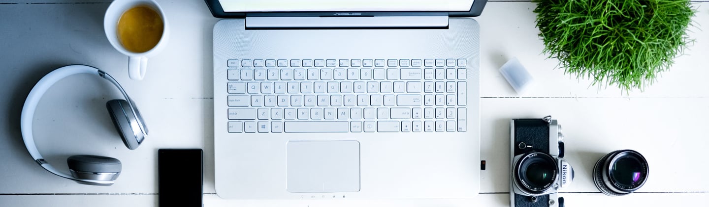 mesa-com-computador-fone-de-ouvido-café-câmera-celular-e-uma-planta-em-cima