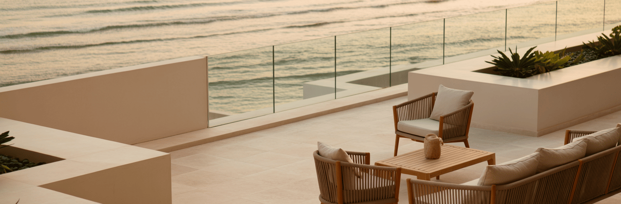 Luxury outdoor patio furniture set on a modern stone terrace with sunset ocean views.