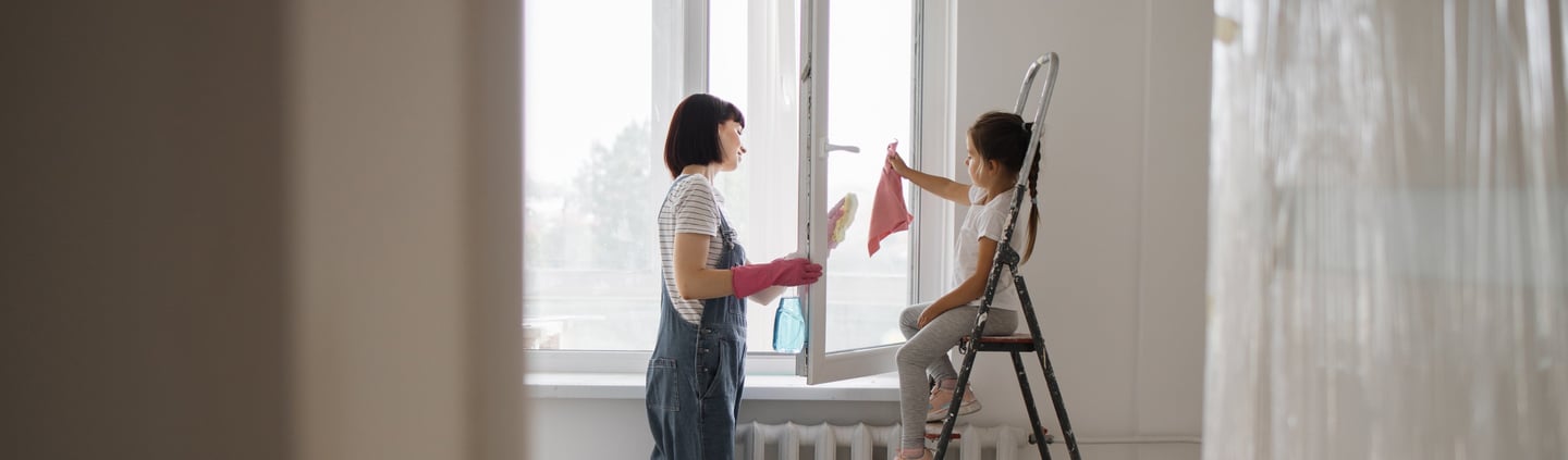 a woman in overalls and a white shirt is painting a window