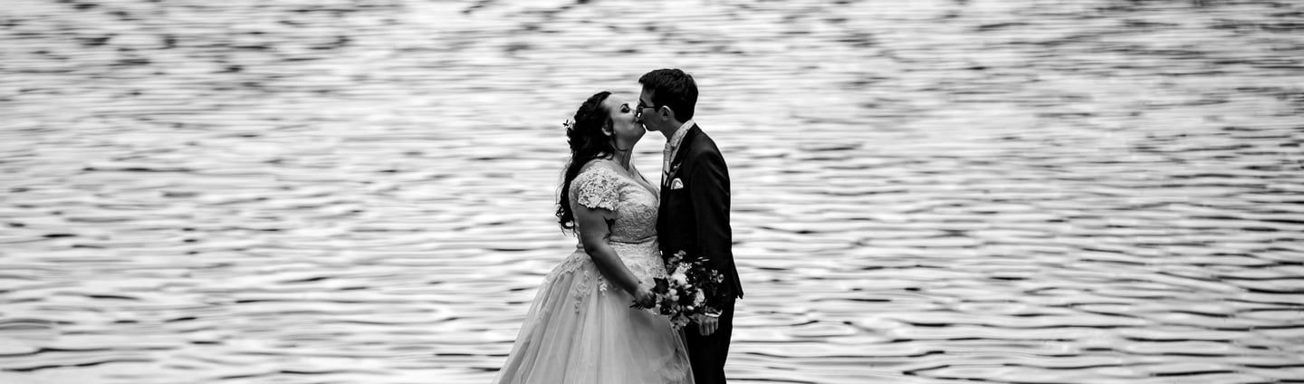 a bride and groom kissing in front of a lake
