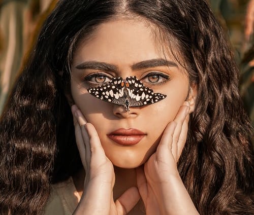 spanish lady holdung fase with 2 hands and butterfly lend on her nose