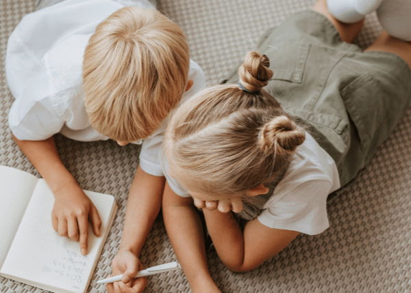 two kids laying on floor and writing