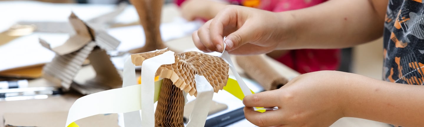 A child sticking paper strips to a concertina cardboard structure.