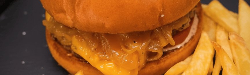 Burger gourmand aux oignons caramélisés, steak juteux et fromage fondu dans un pain bun doré.