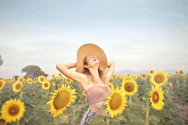 A joyful woman in straw hat standing in a sunflower field with arms outstretched, embracing the sun