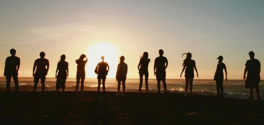 group of people standing on a beach at sunset